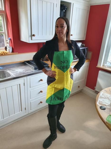 A woman in a kitchen wearing a Jamaican flag apron with "NO PROBLEM" written on it.