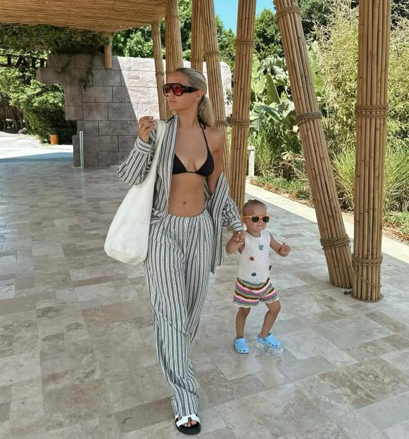 Woman in striped pants and bikini top walking with toddler.