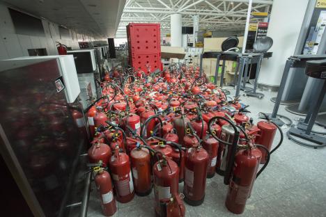 Many fire extinguishers in a mostly empty airport terminal.