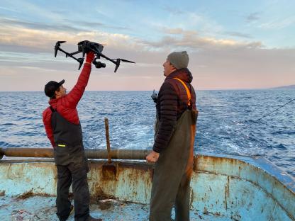Two men on a boat operating a drone over the ocean.