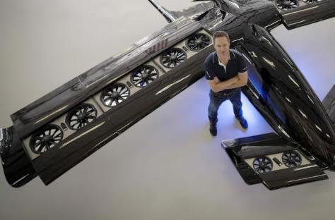 A man stands with arms crossed in front of the Cavorite X7 aircraft.