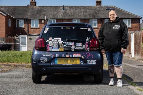 Woman standing next to her car covered in bumper stickers, one of which caused her to be charged with displaying abusive writing.