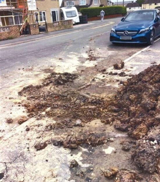 Dirty, excavated debris on a building site next to a road with houses and a car.