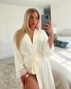 Woman in a white satin robe with lace cuffs taking a selfie.