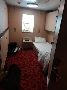 Small ship cabin with a single bed and overhead bunks.