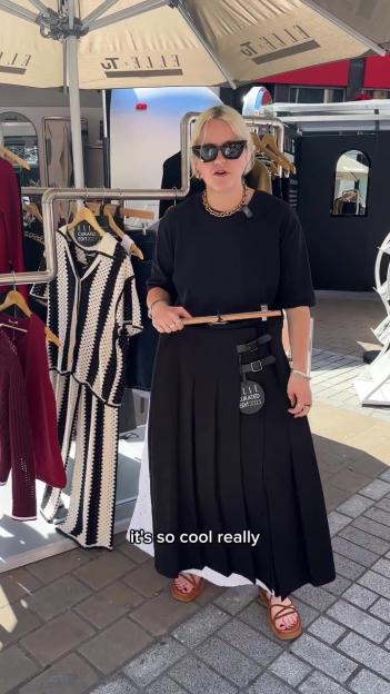 Woman standing in front of clothing rack, showcasing a black skirt.