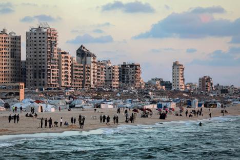 Displaced people at a temporary shelter on a beach near damaged buildings in Gaza City.