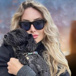 Woman in sunglasses holding a small black dog.