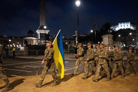 Ukrainian soldiers carrying their nation's flag march at night.