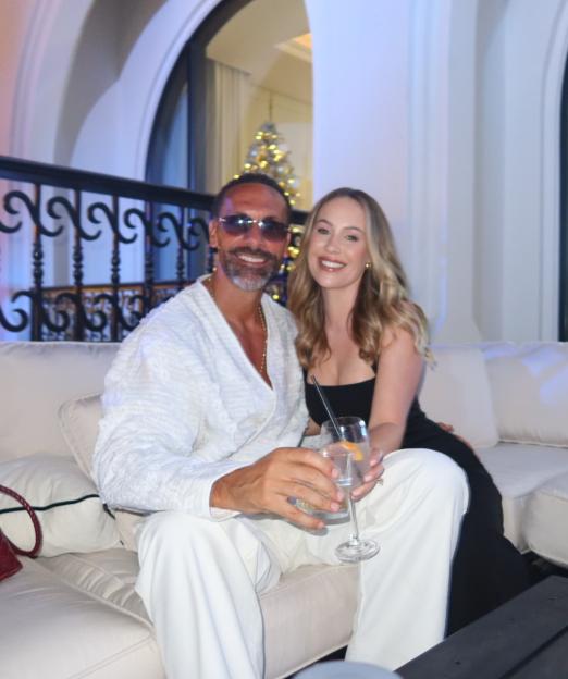 Kate Ferdinand and a man sitting on a couch, holding drinks.