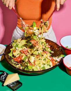 Person tossing a chopped salad with salami and chickpeas.