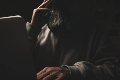 A man with a beard sits at a laptop at night.