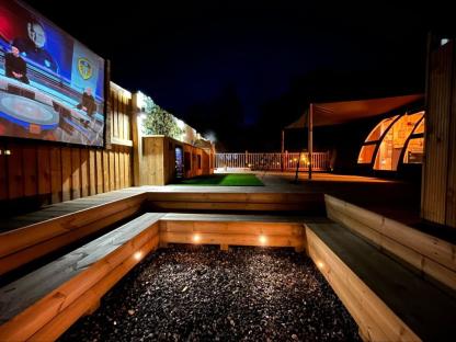 Luxury glamping tent with outdoor cinema and pizza oven at night.