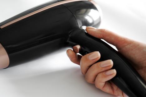 A hand holding a black and rose gold hair dryer.