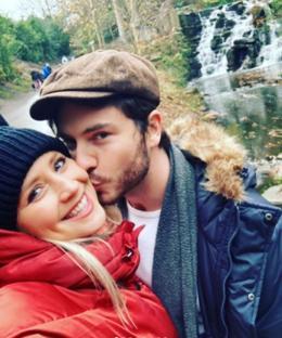 Amy Walsh and Toby Alexander Smith kissing in a park near a waterfall.