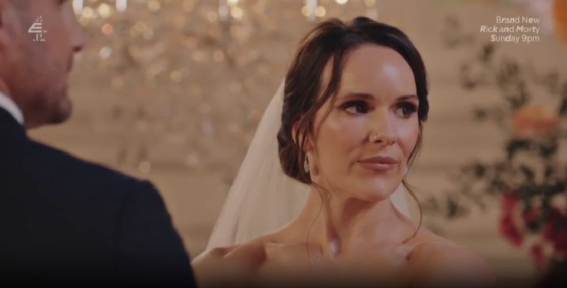 A bride wearing a veil and a strapless dress looks towards a man whose back is to the camera.