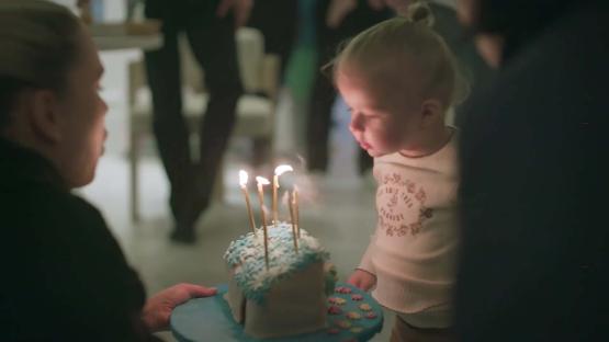 Toddler blowing out candles on a birthday cake.
