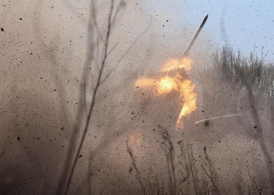 A BM-21 Grad rocket launching with a fiery exhaust and a cloud of dust and debris.