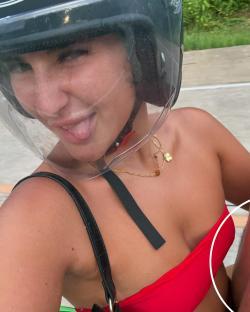 Woman wearing a motorcycle helmet and red bikini top sticking her tongue out.
