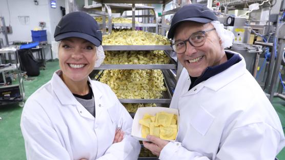 Two people in a pasta factory holding a container of ravioli.