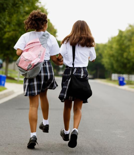 Rear view of two schoolgirls holding hands and walking down a street.