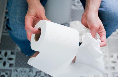Person sitting on a toilet holding toilet paper.