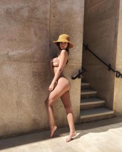 Emily Ratajkowski topless, wearing a straw hat, standing near a staircase.