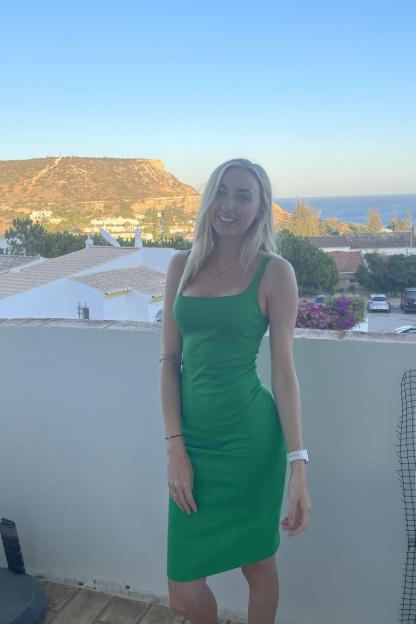 Woman in green dress on balcony overlooking ocean and hills.