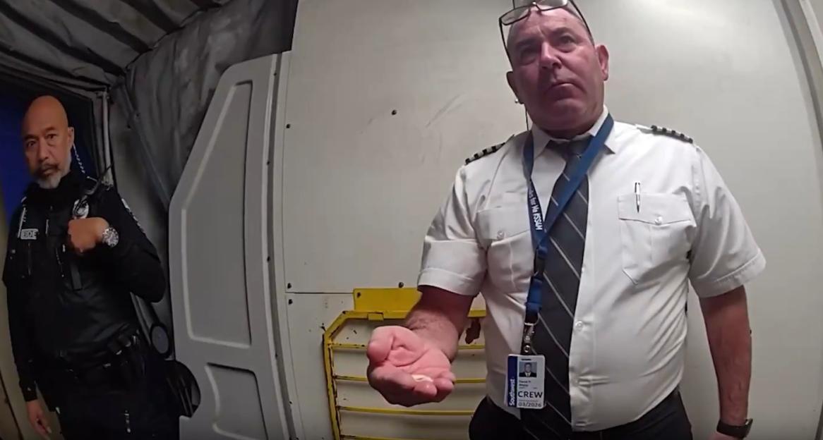 A pilot being escorted from a cockpit by security.