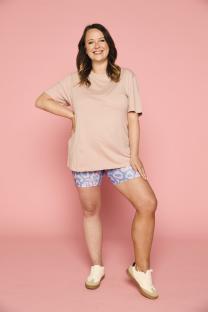 Woman in pink shirt and patterned shorts smiling against a pink background.