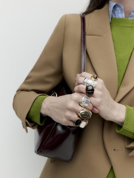 Hands with multiple rings holding a dark red handbag.