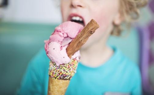 Child eating strawberry ice cream cone with sprinkles and a chocolate bar.
