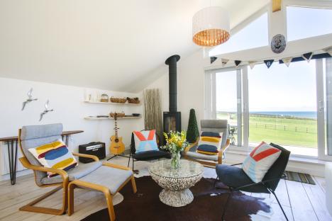 Living room with ocean view, wood-burning stove, and colorful seating.