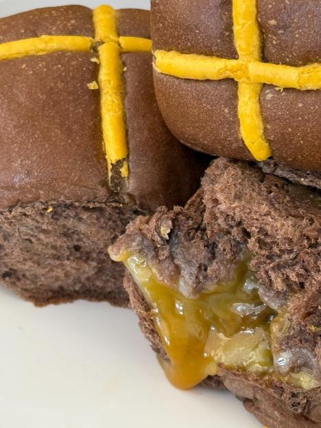 Chocolate hot cross buns with a yellow filling.