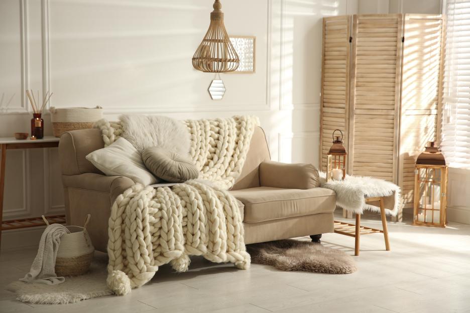 Cozy living room with beige sofa, knitted blanket, and cushions.