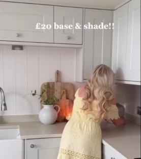 Woman in yellow dress showing off a £20 table lamp.