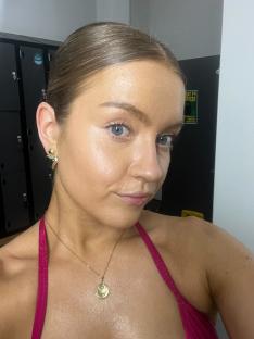 Woman with light makeup and hair pulled back, wearing a pink top and gold necklace.