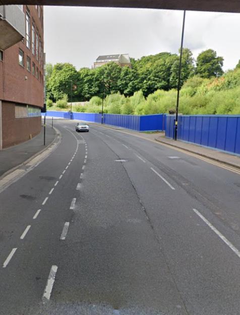 Street scene with a car driving past a blue construction fence.