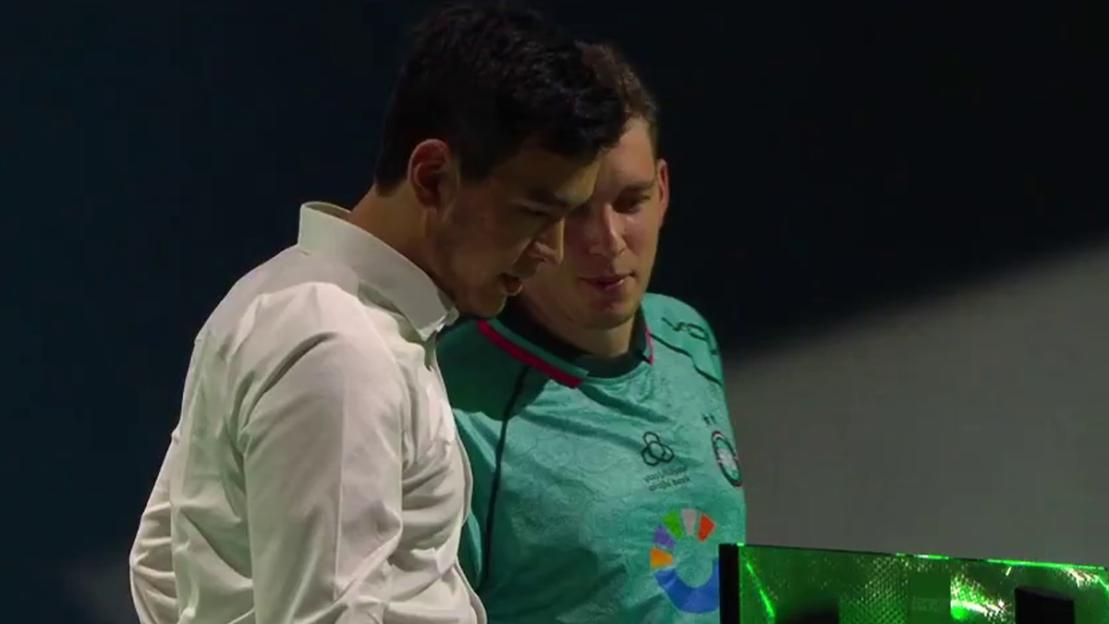 Two men in discussion.  One man is wearing a white shirt, the other a teal jersey.