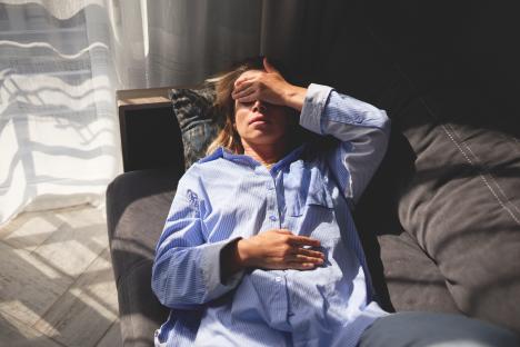 Woman lying on a couch, hand on forehead, appearing stressed.