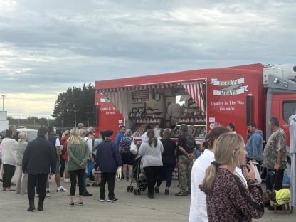 A crowd of people waiting in line at Perry's Meats market, a red food truck.
