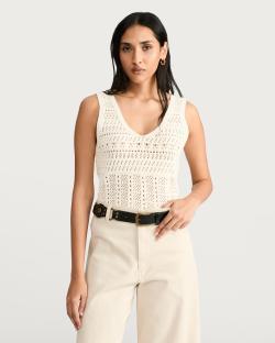 Woman wearing a cream crocheted sleeveless top and cream pants.