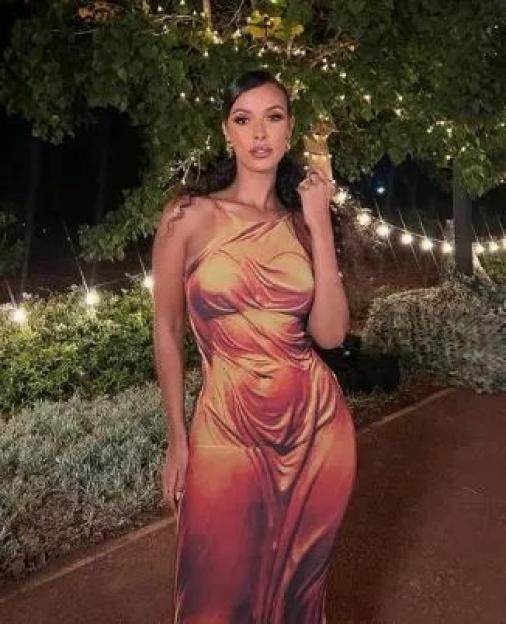 A woman in an orange and red patterned dress stands outside at night.