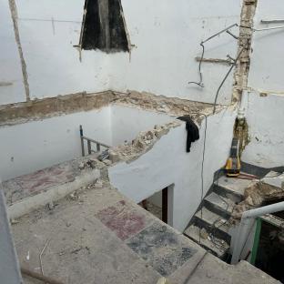 Demolition of a building interior, showing rubble, exposed pipes, and a staircase.