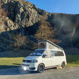 White campervan parked in front of a rocky hillside.