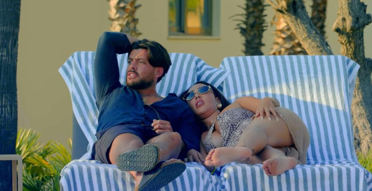 Screenshot of a man and woman relaxing on lounge chairs by a pool.