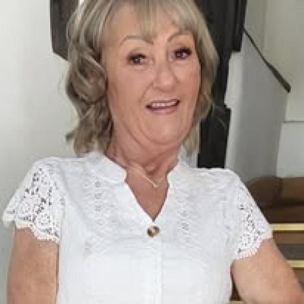 Portrait of a woman with short, wavy blonde hair wearing a white lace top.