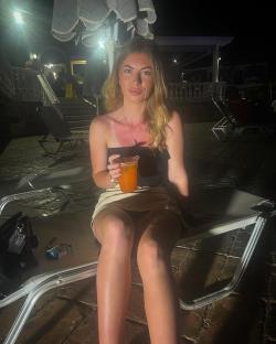 Woman sitting on a lounge chair at night holding a drink.