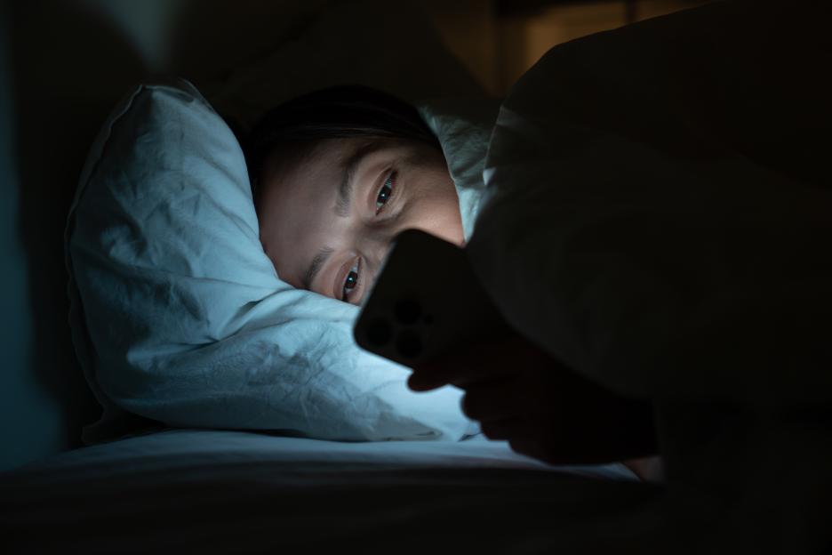 Female having insomnia, sleeping disorder lying in bed with smartphone, surfing in internet at night