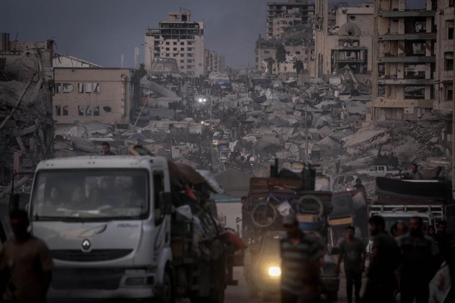 Palestinians, including children, in Gaza City center migrate towards southern regions with belongings amidst destroyed buildings and a makeshift tent city.